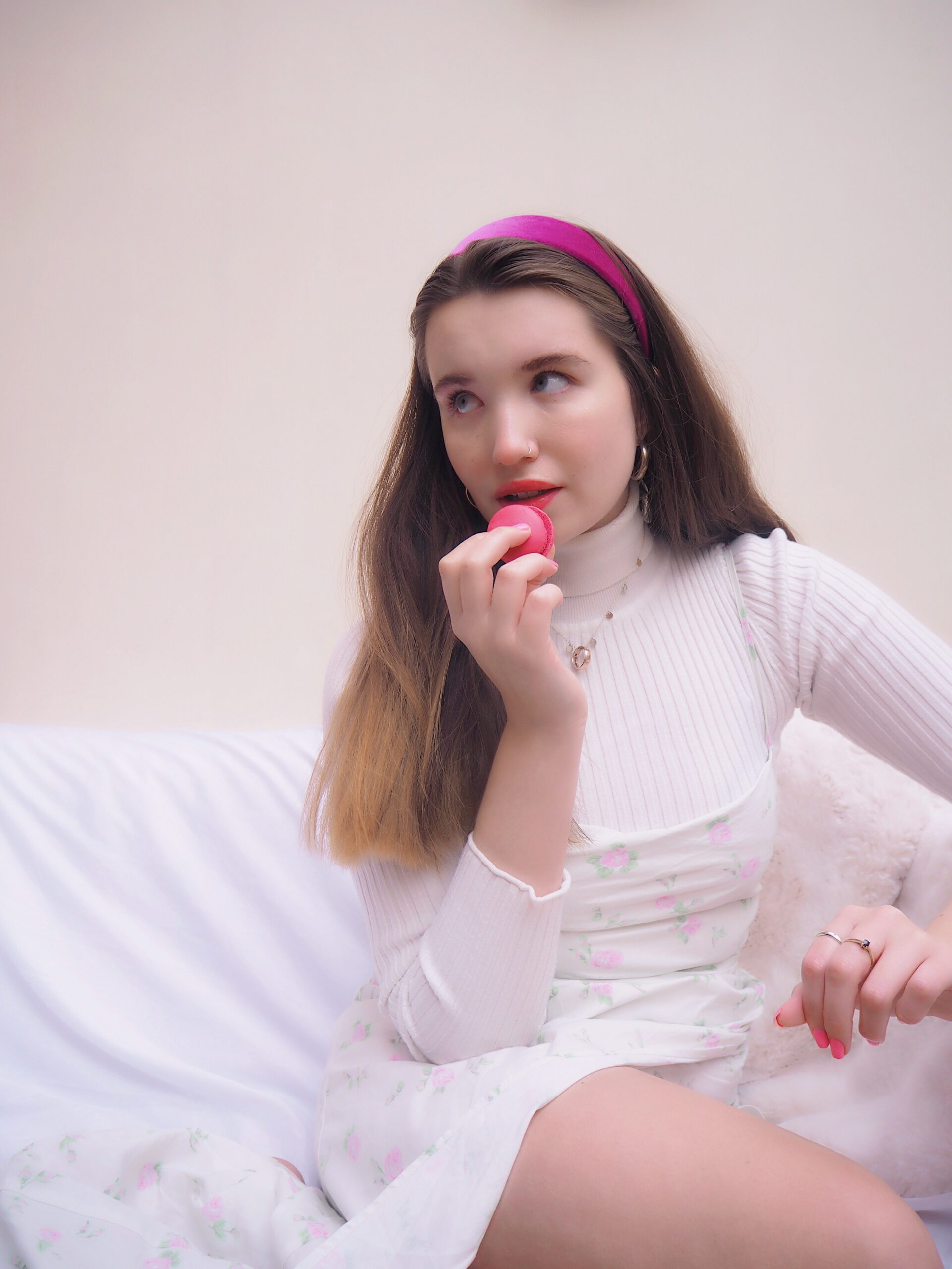 wedding copywriter eating a pink macron while sitting on the sofa in a white dress