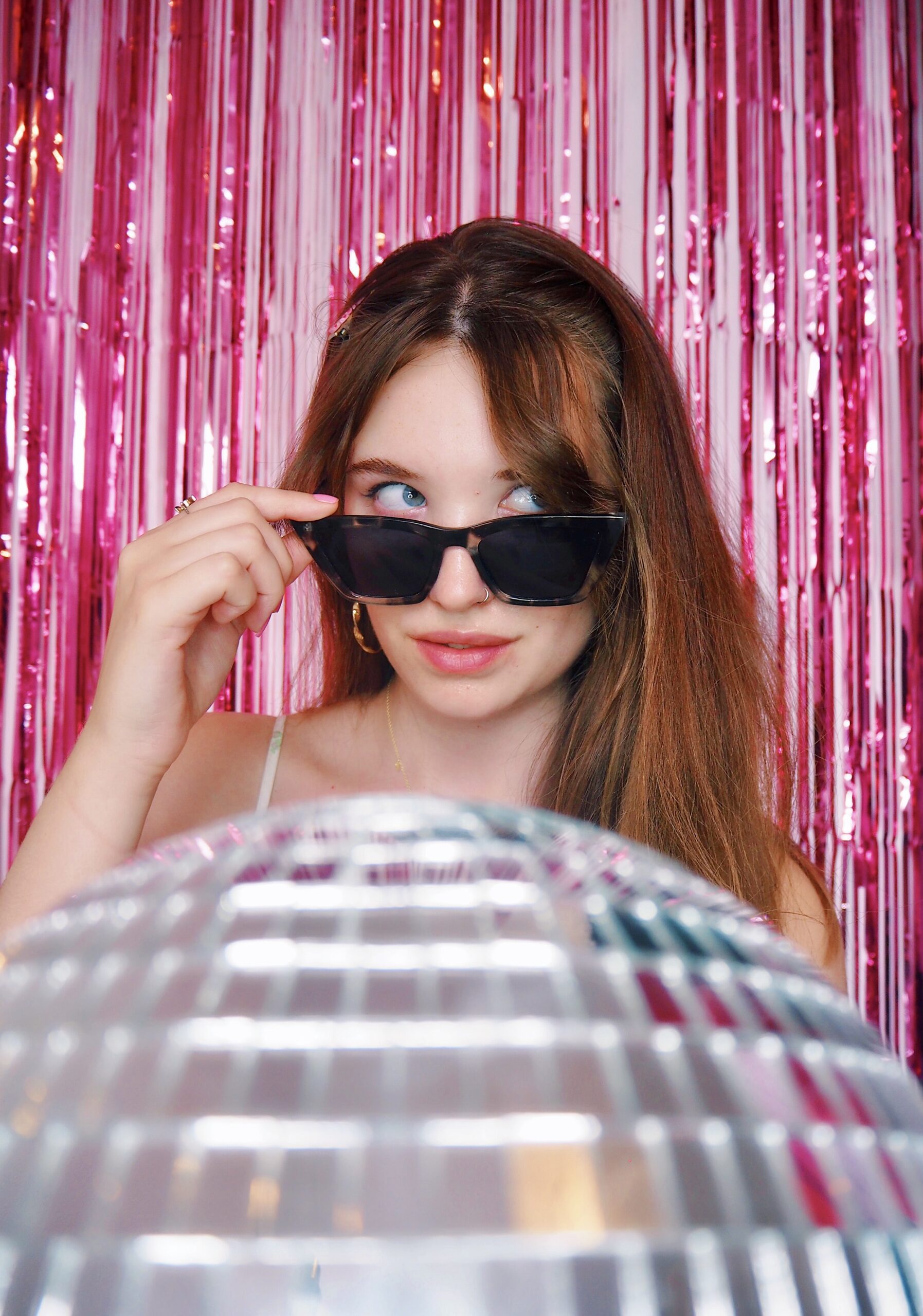 Website copywriter wearing black sunglasses, gazing upwards, sat behind a silver disco ball