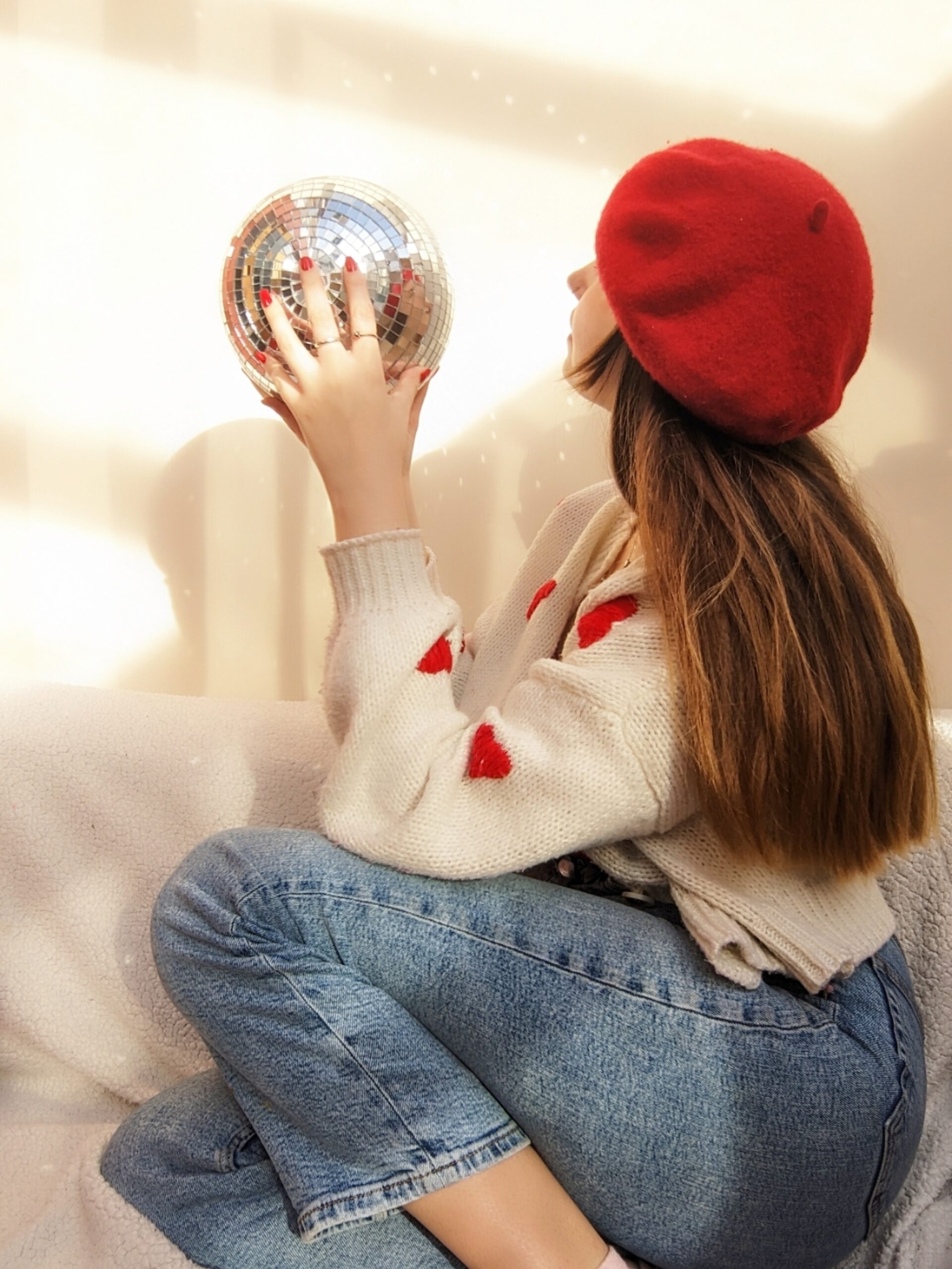 Girl wearing red beret and holding a disco ball stars up at a white wall