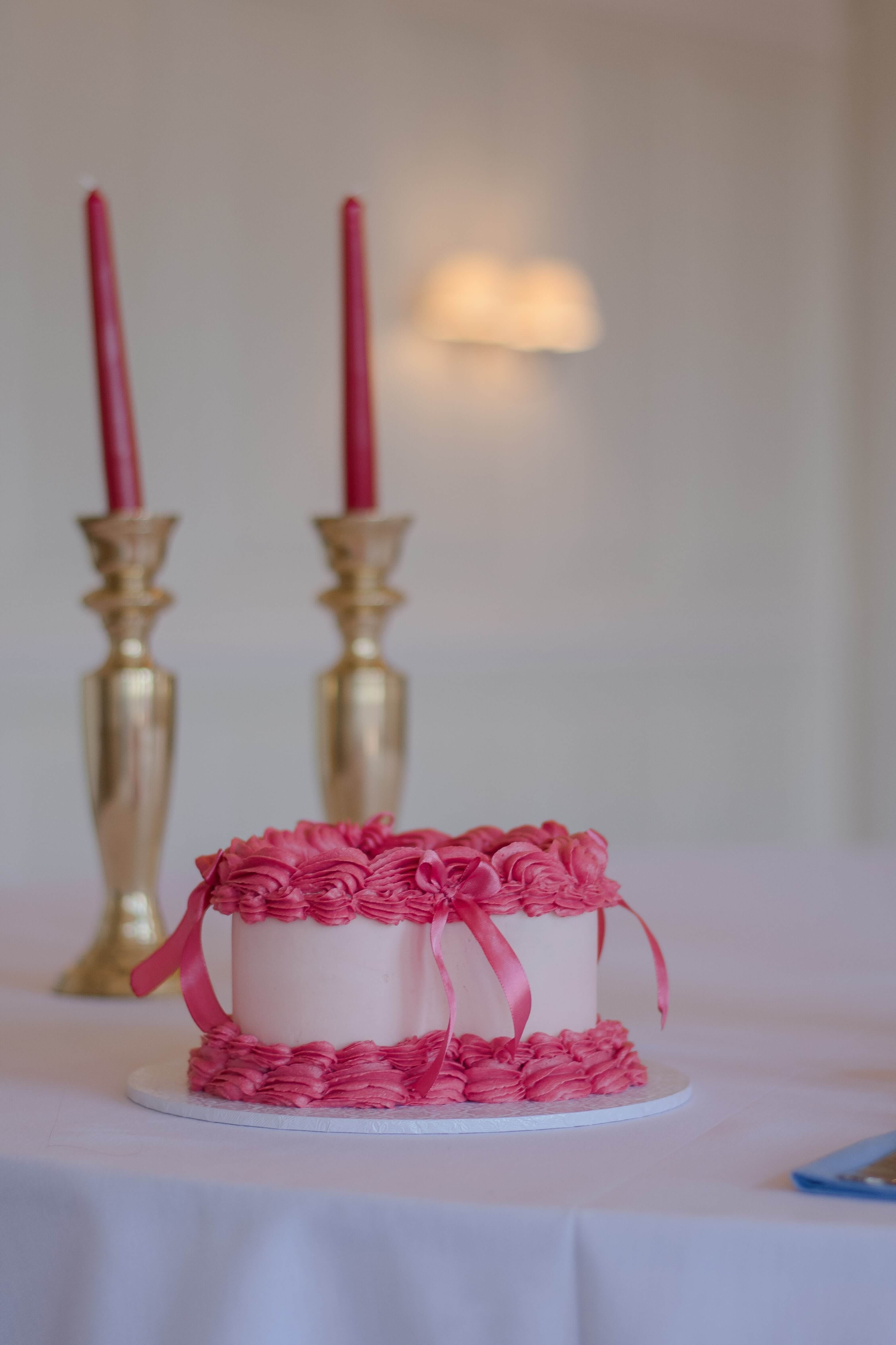 Wedding tablescape with a white table, pink heart-shaped cake, gold candle stick holders and red candles.